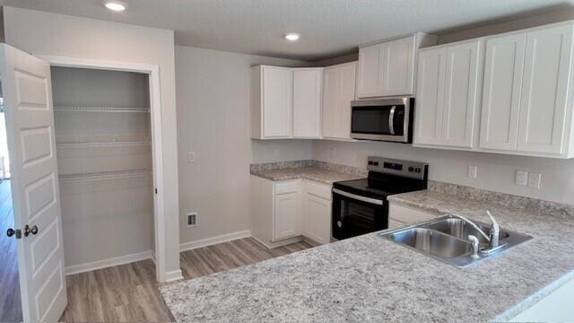 kitchen with white cabinets, sink, light wood-type flooring, kitchen peninsula, and stainless steel appliances