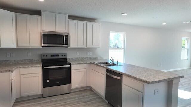 kitchen with kitchen peninsula, stainless steel appliances, sink, light hardwood / wood-style flooring, and white cabinets