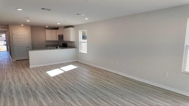 kitchen with white cabinets, light wood-type flooring, kitchen peninsula, and sink