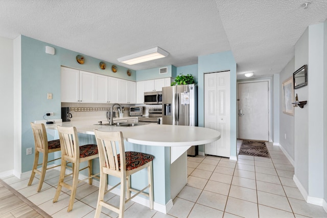 kitchen with kitchen peninsula, appliances with stainless steel finishes, a kitchen breakfast bar, a textured ceiling, and white cabinetry