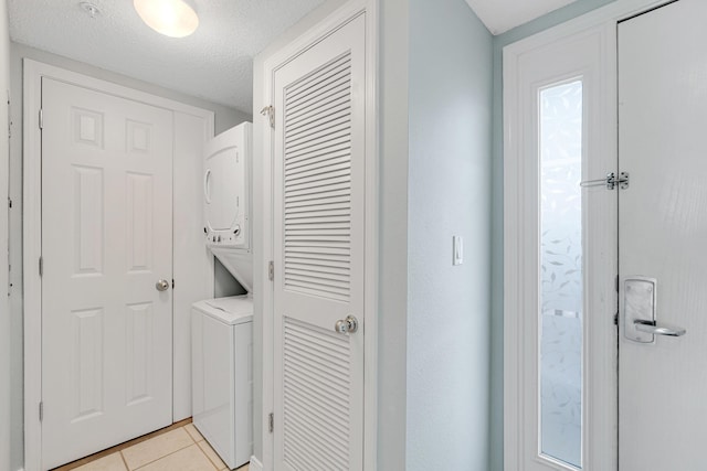 laundry room featuring a textured ceiling, stacked washing maching and dryer, and light tile patterned flooring