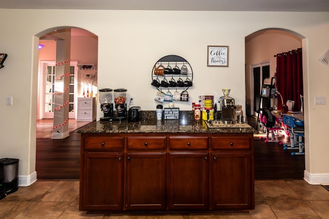 bar with dark wood-type flooring and dark stone counters