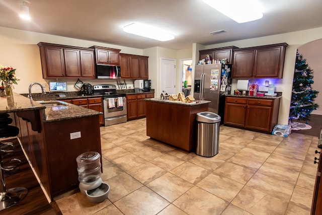 kitchen featuring a breakfast bar, dark stone counters, sink, appliances with stainless steel finishes, and kitchen peninsula