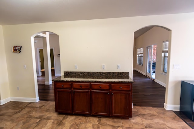 kitchen with arched walkways, baseboards, dark stone counters, and dark brown cabinets