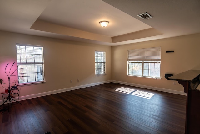 unfurnished room with dark wood-style floors, a raised ceiling, visible vents, and baseboards