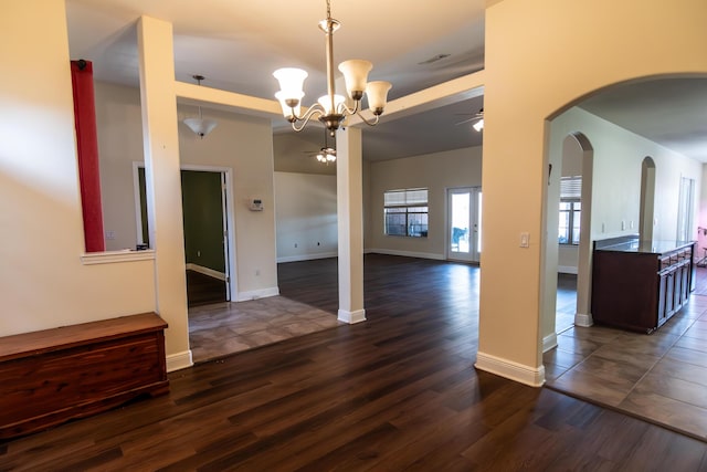 unfurnished dining area with arched walkways, ceiling fan with notable chandelier, dark wood-type flooring, visible vents, and baseboards