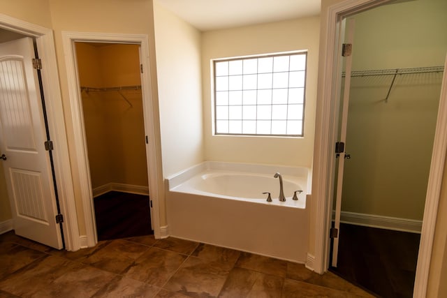 full bathroom with a walk in closet, baseboards, and a bath