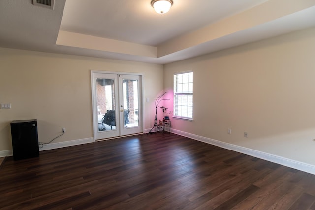 spare room with dark wood-type flooring, a tray ceiling, and french doors