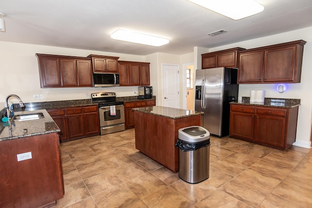 kitchen featuring a center island, visible vents, appliances with stainless steel finishes, a sink, and dark stone counters