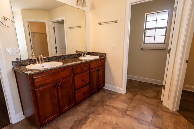 full bath featuring double vanity, a spacious closet, a sink, and baseboards