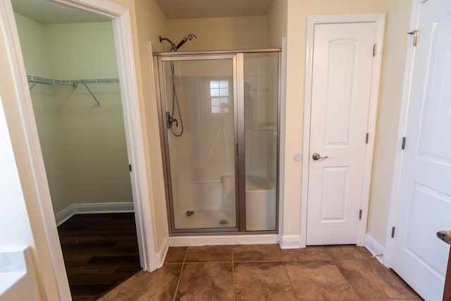 full bathroom with a stall shower, a walk in closet, and baseboards