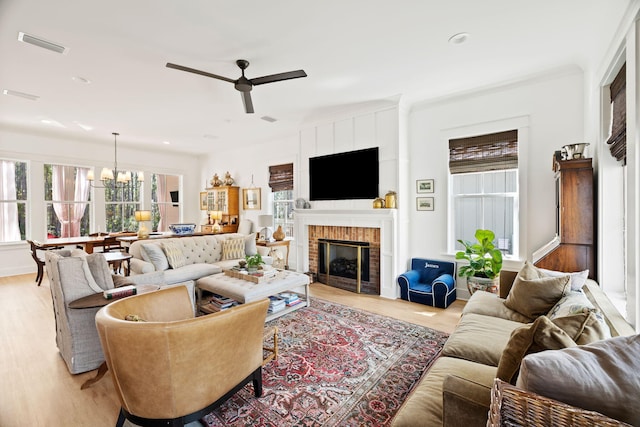 living room with ceiling fan with notable chandelier, light hardwood / wood-style flooring, and a brick fireplace