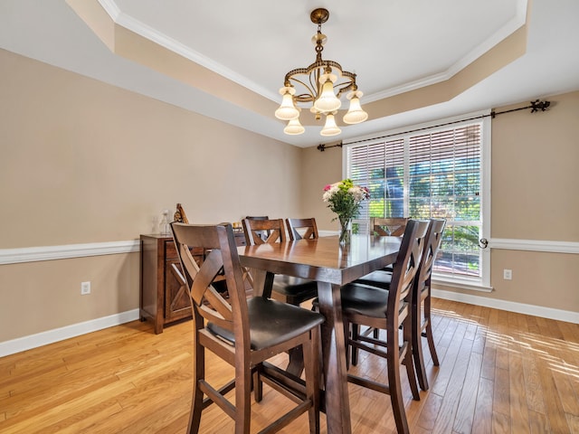 dining area with a raised ceiling, light hardwood / wood-style flooring, and an inviting chandelier