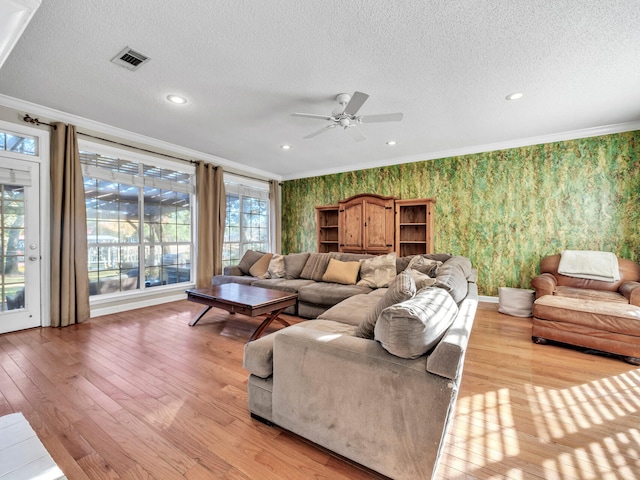 living room featuring a textured ceiling, ceiling fan, light wood-type flooring, and ornamental molding