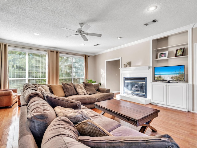 living room featuring a textured ceiling, light hardwood / wood-style floors, ornamental molding, and a tiled fireplace