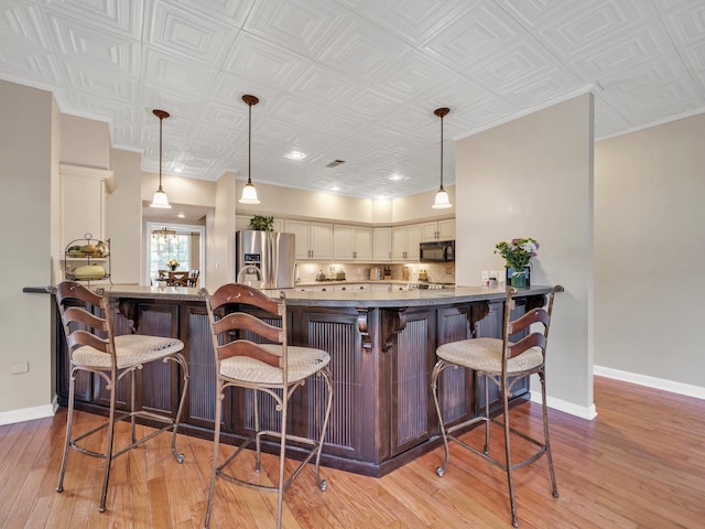 kitchen featuring stainless steel fridge, decorative light fixtures, and light wood-type flooring