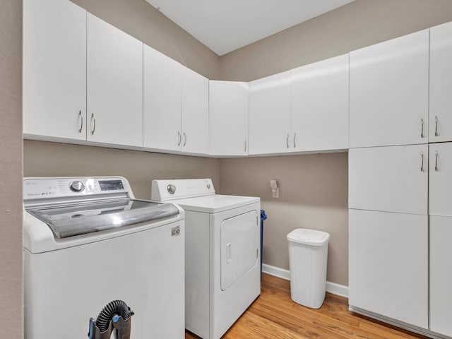 clothes washing area with cabinets, washing machine and dryer, and light hardwood / wood-style flooring