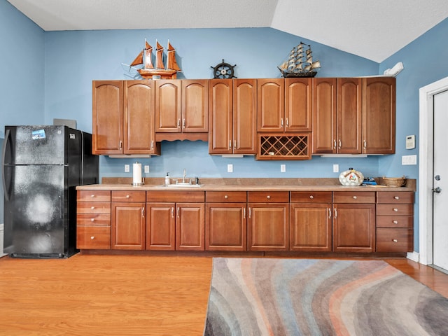 kitchen featuring black fridge, sink, light hardwood / wood-style floors, and vaulted ceiling