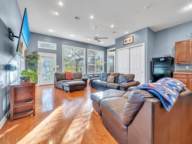 living room featuring ceiling fan, light hardwood / wood-style flooring, and a textured ceiling