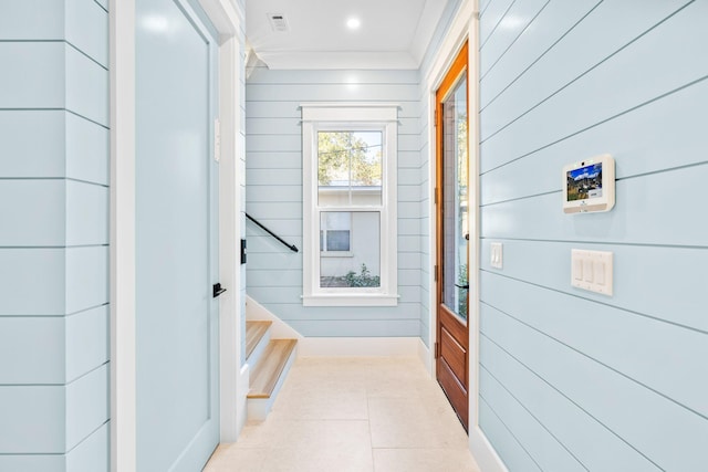 hallway with light tile patterned flooring, ornamental molding, and wooden walls