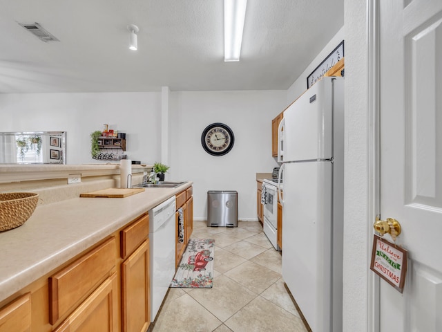 kitchen featuring a textured ceiling, white appliances, sink, and light tile patterned floors