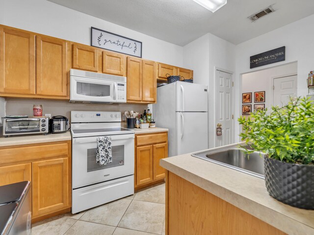 kitchen featuring light tile patterned floors, white appliances, and sink