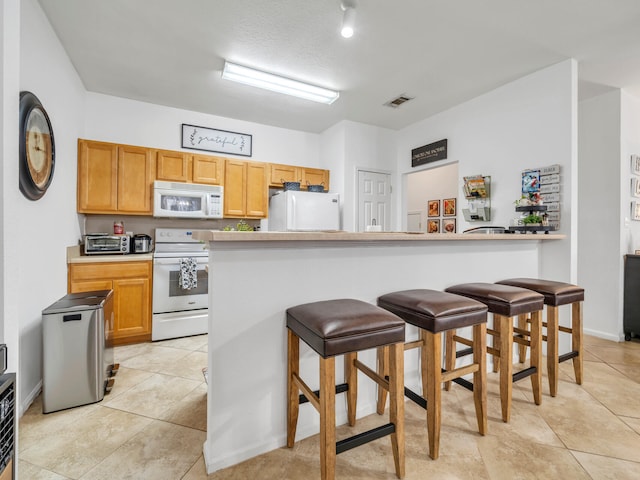 kitchen with a breakfast bar, white appliances, and light tile patterned flooring