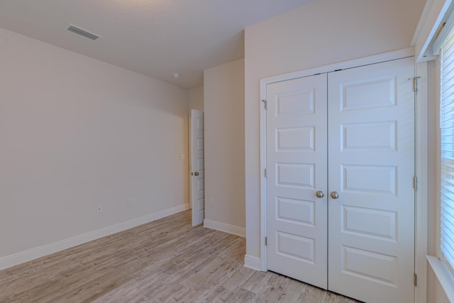 unfurnished bedroom featuring multiple windows, light hardwood / wood-style floors, and a closet