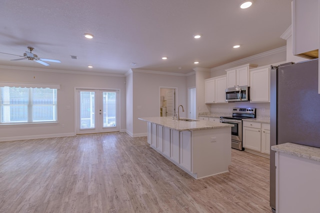 kitchen with stainless steel appliances, an island with sink, white cabinets, and light stone counters