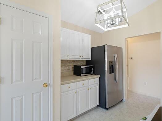 kitchen featuring white cabinetry, backsplash, stainless steel fridge, a chandelier, and decorative light fixtures