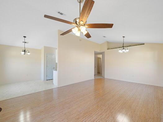 spare room with light hardwood / wood-style flooring, ceiling fan with notable chandelier, and lofted ceiling