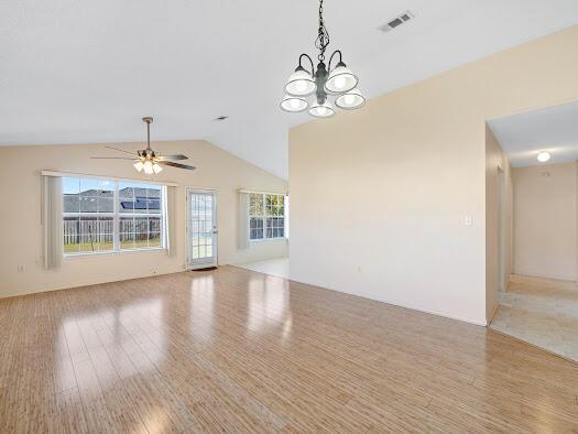 unfurnished living room featuring ceiling fan with notable chandelier, light hardwood / wood-style floors, and lofted ceiling