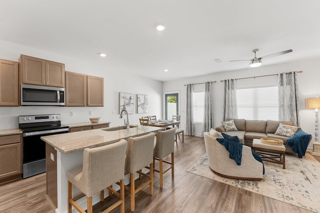 kitchen with a breakfast bar, sink, appliances with stainless steel finishes, light hardwood / wood-style floors, and light stone counters