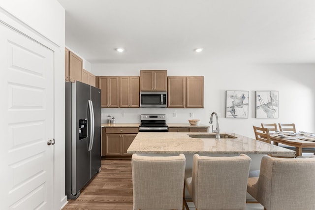 kitchen with dark wood-type flooring, sink, an island with sink, appliances with stainless steel finishes, and light stone counters