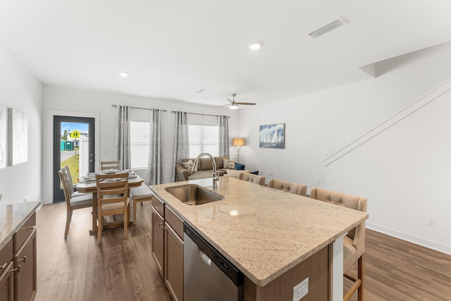 kitchen featuring light stone counters, stainless steel dishwasher, sink, dark hardwood / wood-style floors, and an island with sink