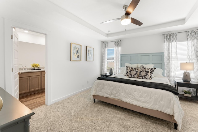 carpeted bedroom featuring ceiling fan, ensuite bathroom, a tray ceiling, and multiple windows