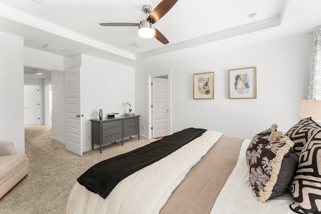 carpeted bedroom with a raised ceiling and ceiling fan