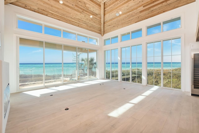 unfurnished sunroom with plenty of natural light, a water view, lofted ceiling, and a view of the beach