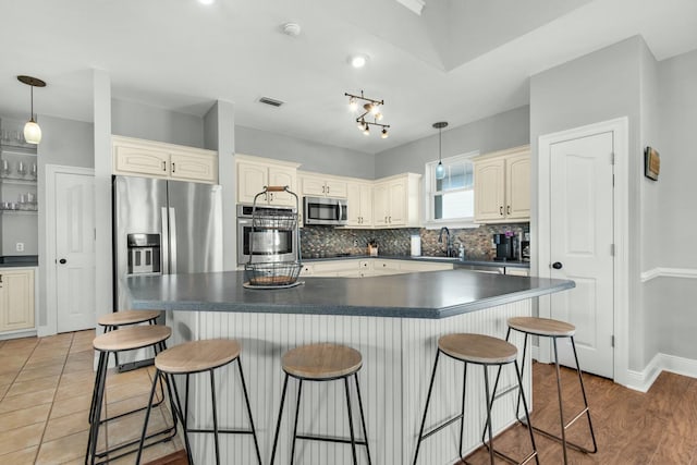 kitchen with hardwood / wood-style floors, a kitchen breakfast bar, hanging light fixtures, appliances with stainless steel finishes, and tasteful backsplash