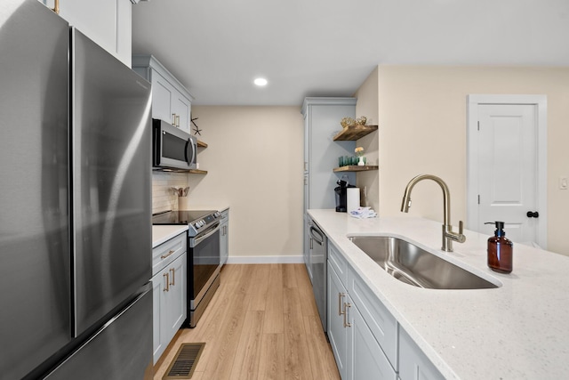 kitchen featuring appliances with stainless steel finishes, backsplash, light stone counters, sink, and light hardwood / wood-style flooring