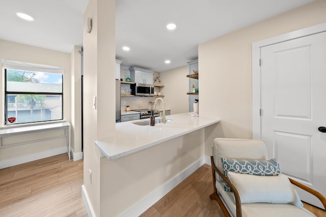 kitchen featuring kitchen peninsula, backsplash, sink, light hardwood / wood-style flooring, and white cabinets