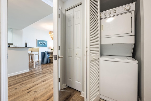 clothes washing area with a chandelier, stacked washing maching and dryer, and light hardwood / wood-style floors