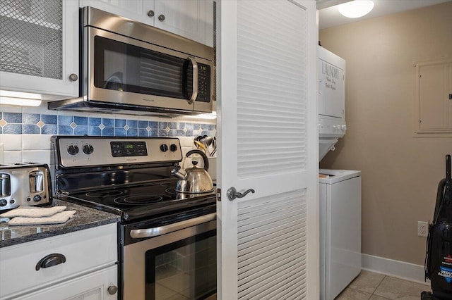 kitchen with stacked washer and dryer, white cabinetry, dark stone countertops, stainless steel appliances, and tasteful backsplash