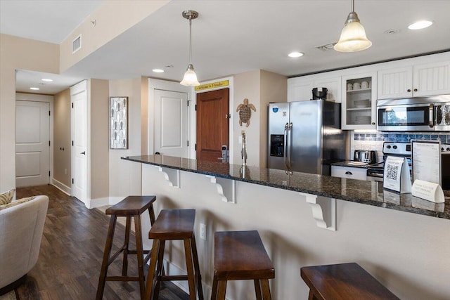 kitchen featuring stainless steel appliances, dark hardwood / wood-style floors, white cabinets, a kitchen bar, and decorative light fixtures