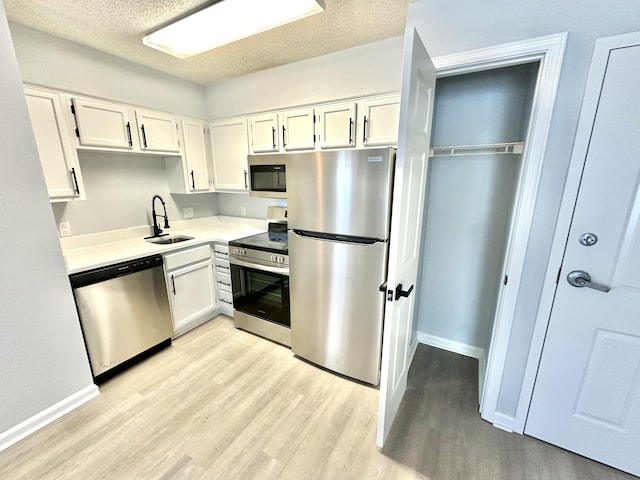 kitchen with sink, appliances with stainless steel finishes, a textured ceiling, white cabinets, and light wood-type flooring