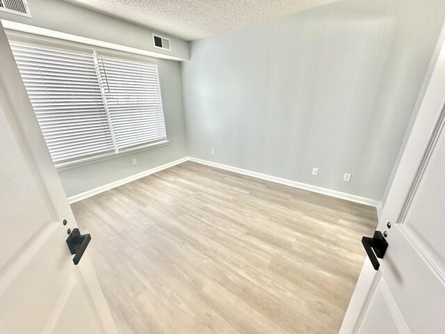 unfurnished room with light hardwood / wood-style flooring and a textured ceiling