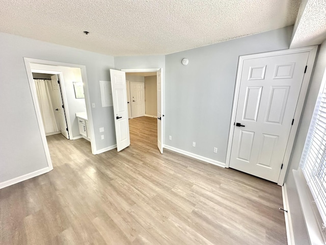 unfurnished bedroom with a textured ceiling, connected bathroom, and light hardwood / wood-style flooring