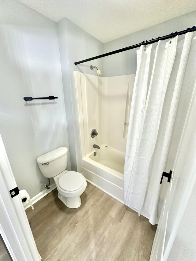 bathroom featuring toilet, shower / bath combo with shower curtain, a textured ceiling, and hardwood / wood-style flooring