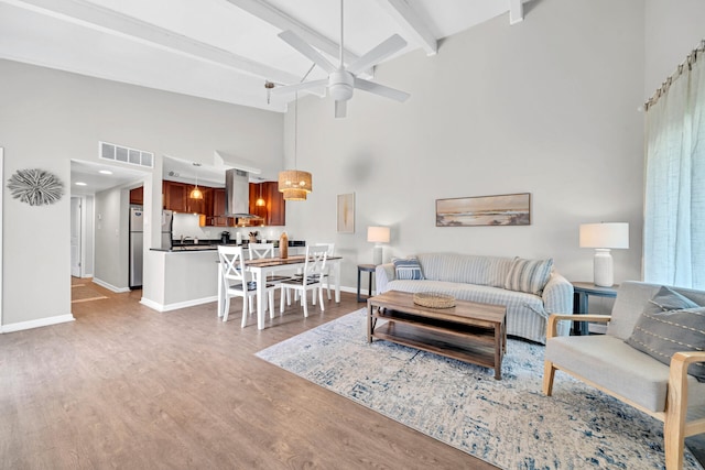 living room featuring beam ceiling, ceiling fan, a towering ceiling, and wood-type flooring