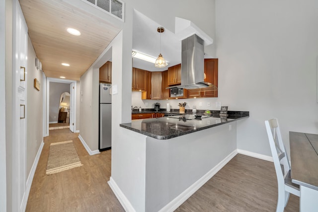 kitchen with island exhaust hood, kitchen peninsula, stainless steel appliances, light hardwood / wood-style flooring, and hanging light fixtures